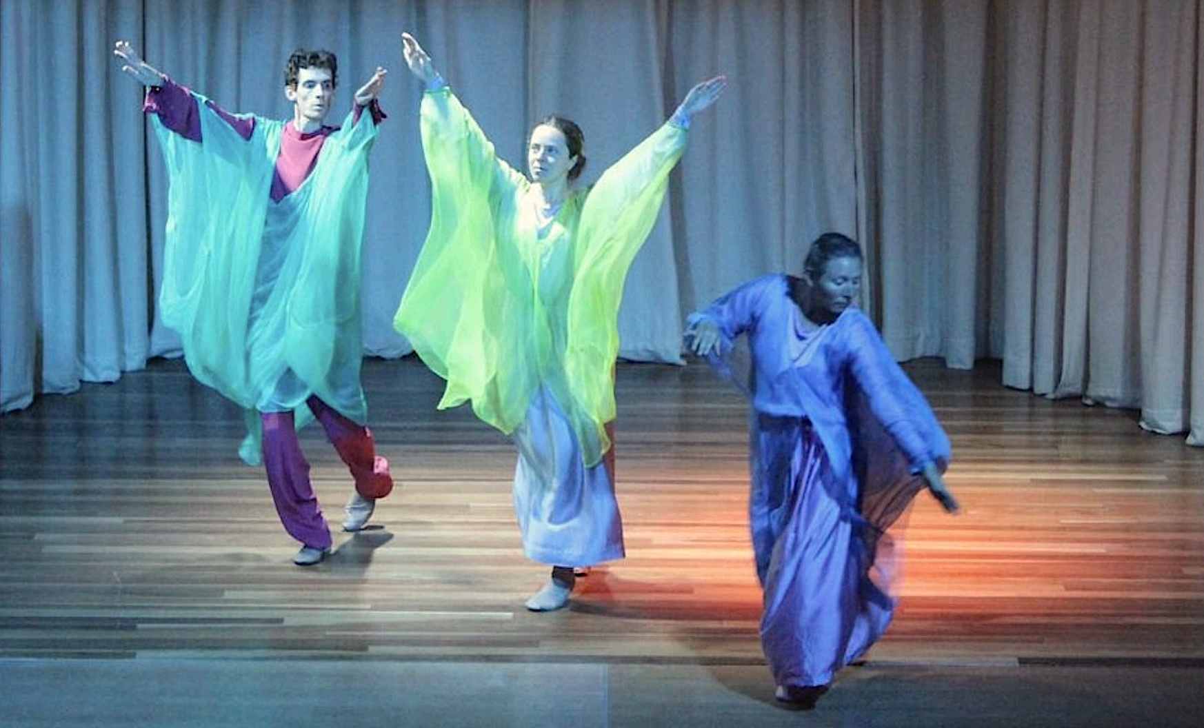 Three people dressed in long floating garments dancing on a stage